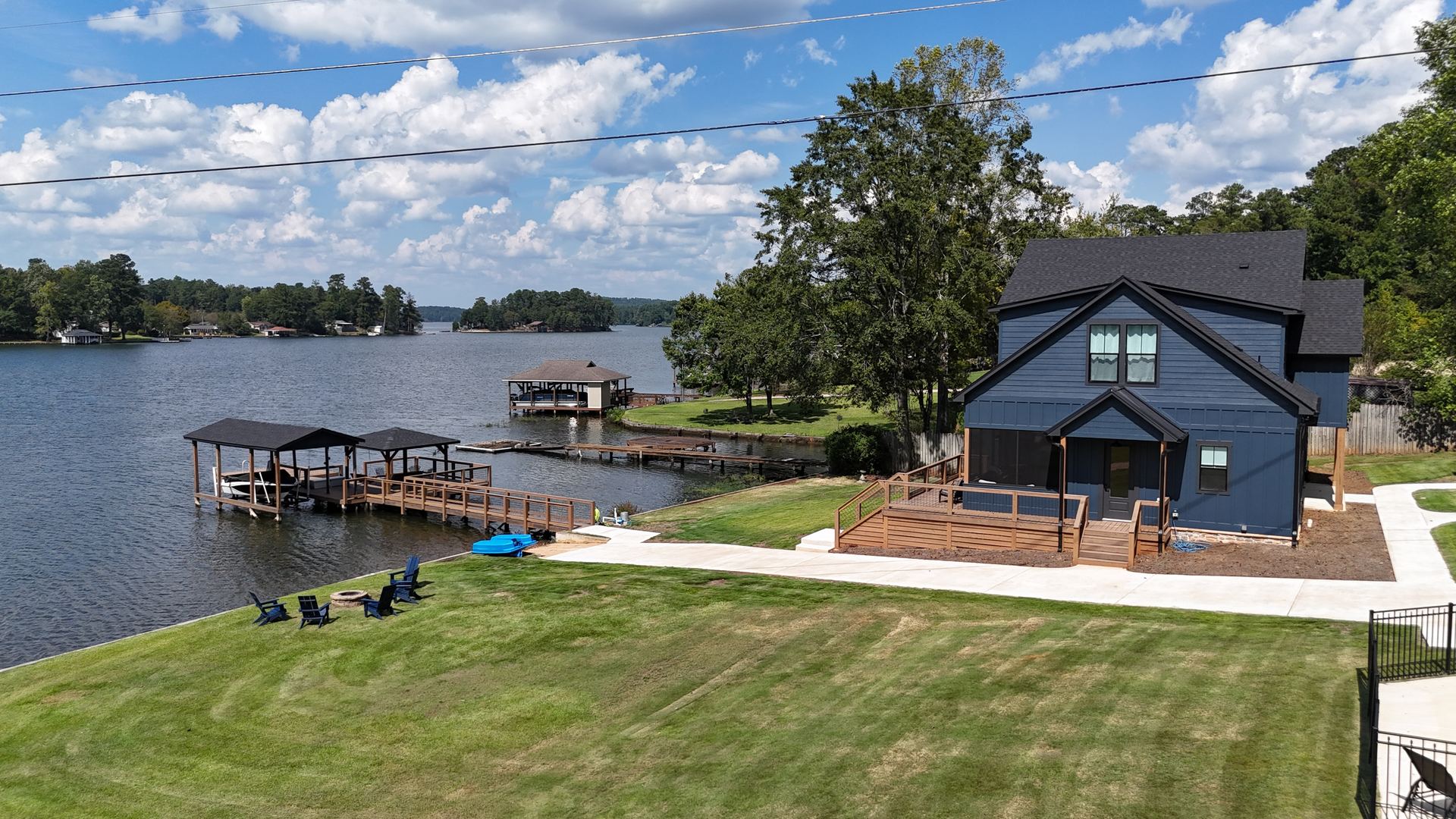 Aerial view of the navy lake house, lawn, dock, fire pit, and kayaks